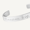 A silver metal cuff bracelet engraved with the phrase 'Dream big.' in a cursive script, shown on a clean white background.