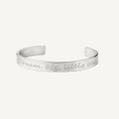 A silver metal cuff bracelet engraved with the inspirational quote 'Dream big, little one' in a cursive font, shown on a clean white background.