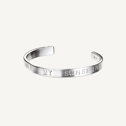 A silver bangle bracelet with the inscription 'You are my sunshine' stamped on it.